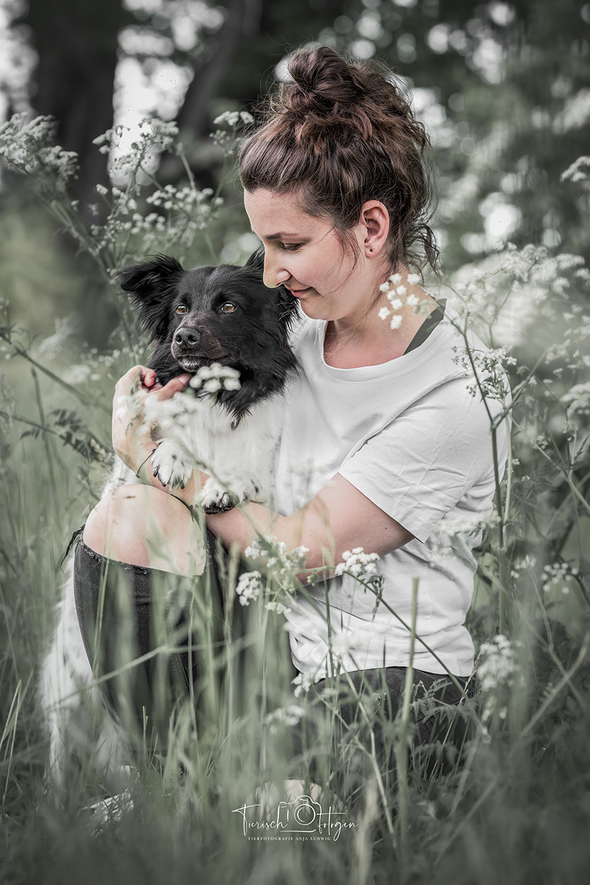 Frau umarmt Border Collie im Gras